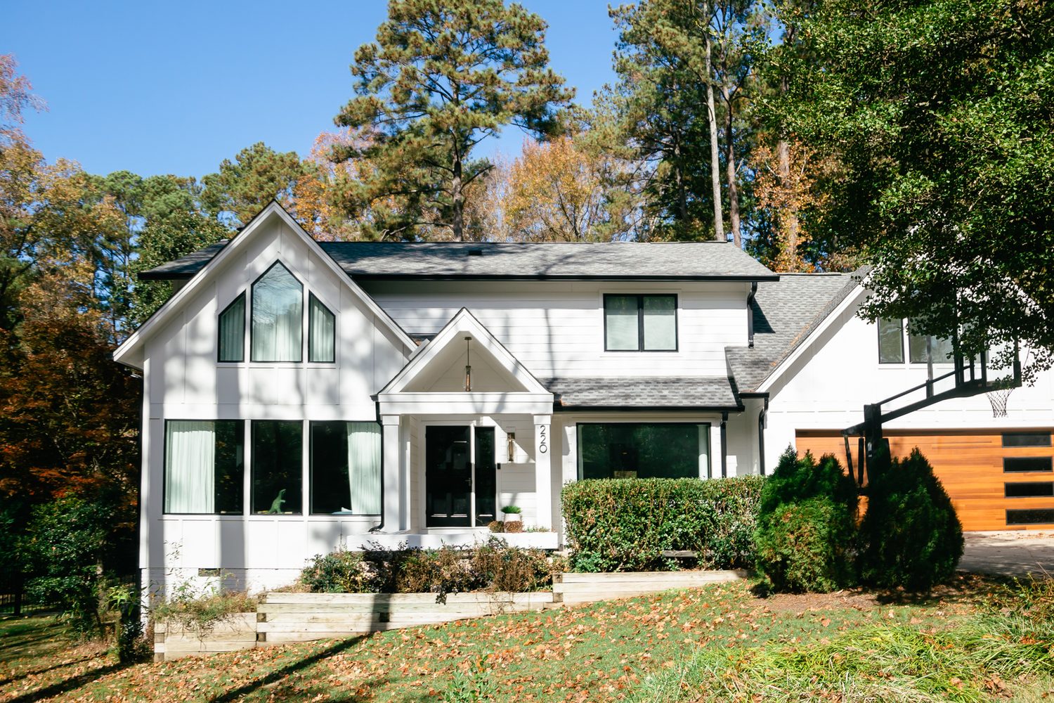After: the same Cary home with new white siding, black-framed windows, and a wood garage door
