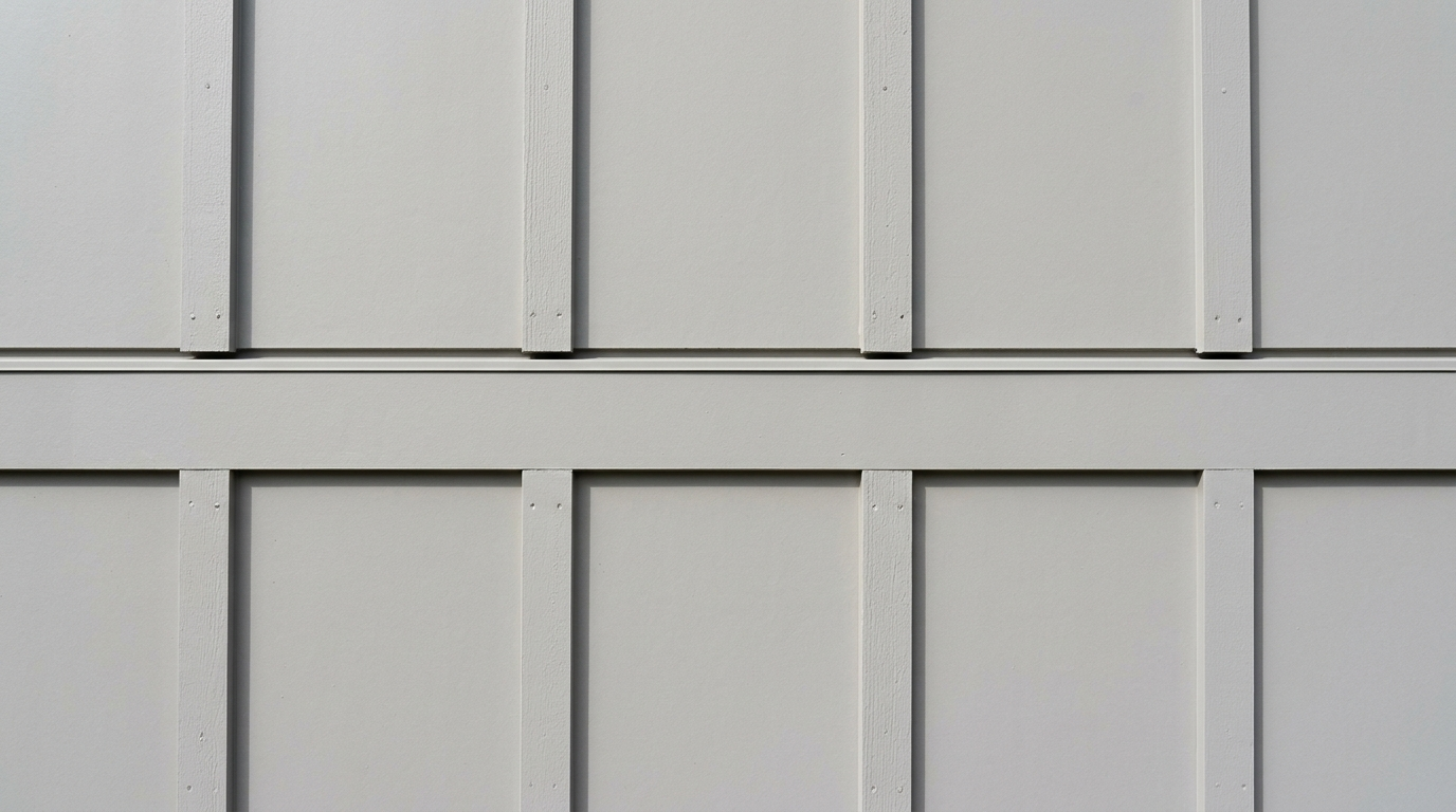 Close-up of a light gray board and batten wall, with vertical battens over flat panels and a horizontal trim band topped by a thin flashing strip where the upper and lower sections meet