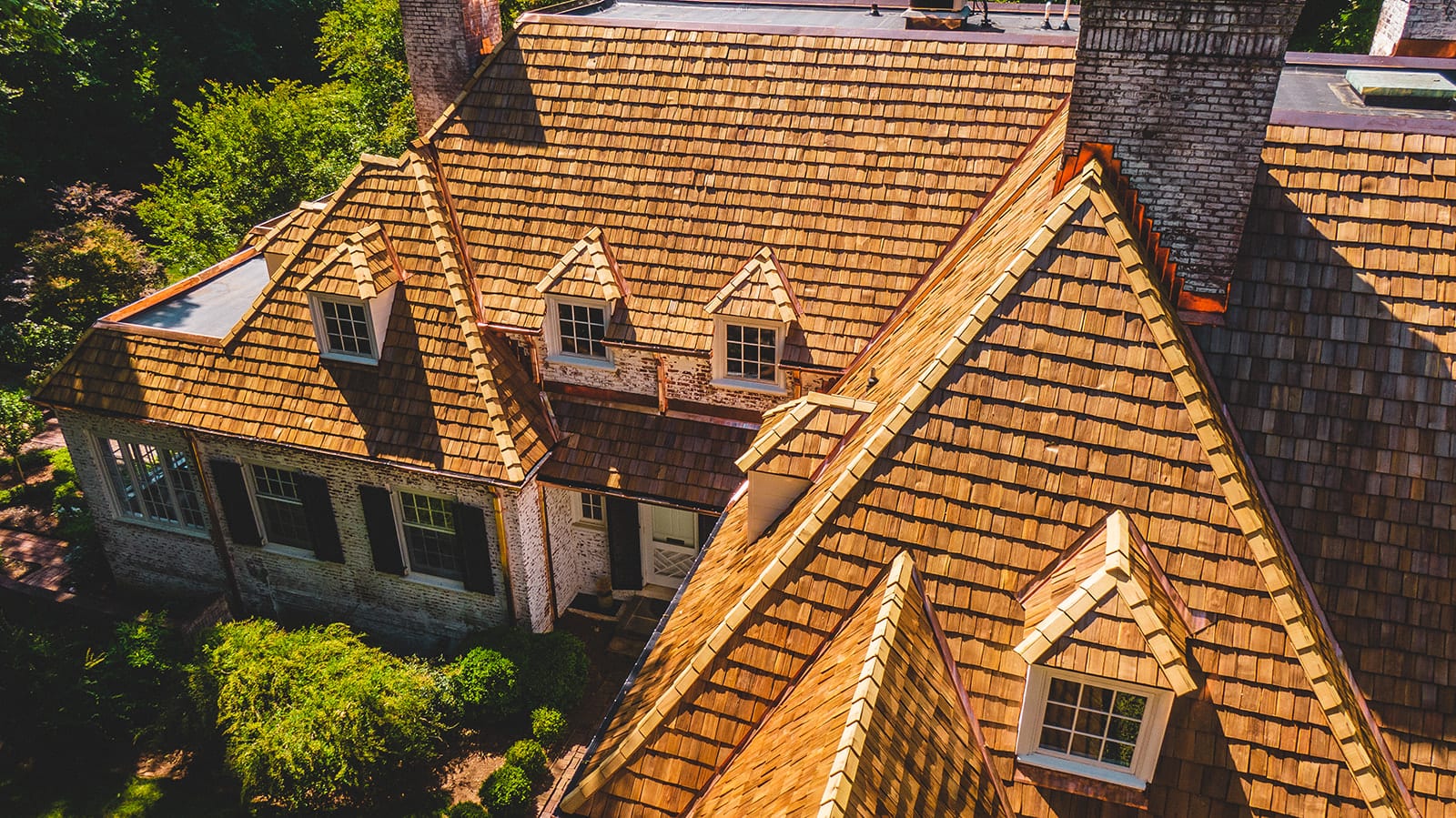 Cedar shake roof with a row of dormers on a stone home among trees