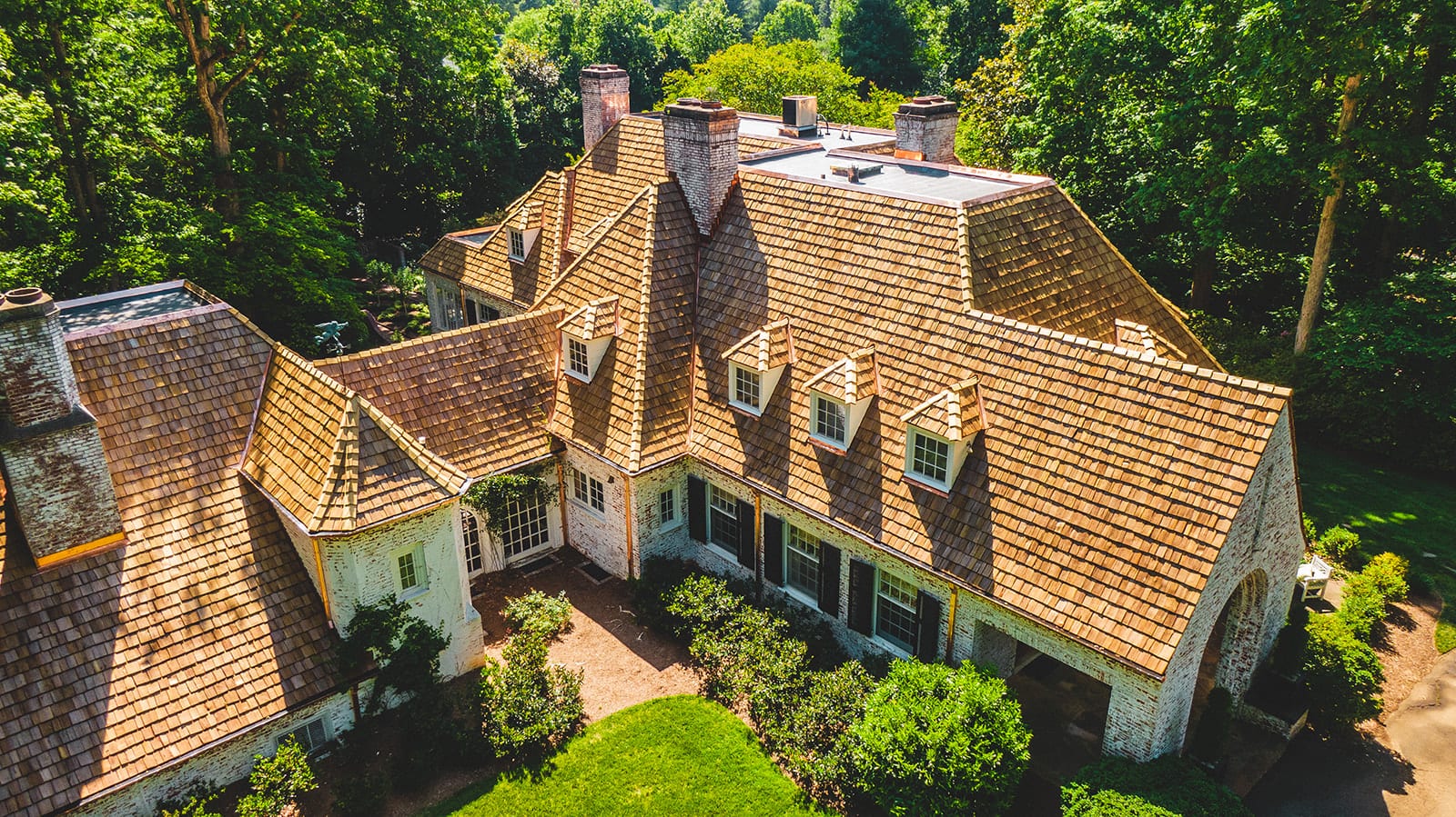 Cedar shake roof with dormers and stone chimneys on a large stone estate home