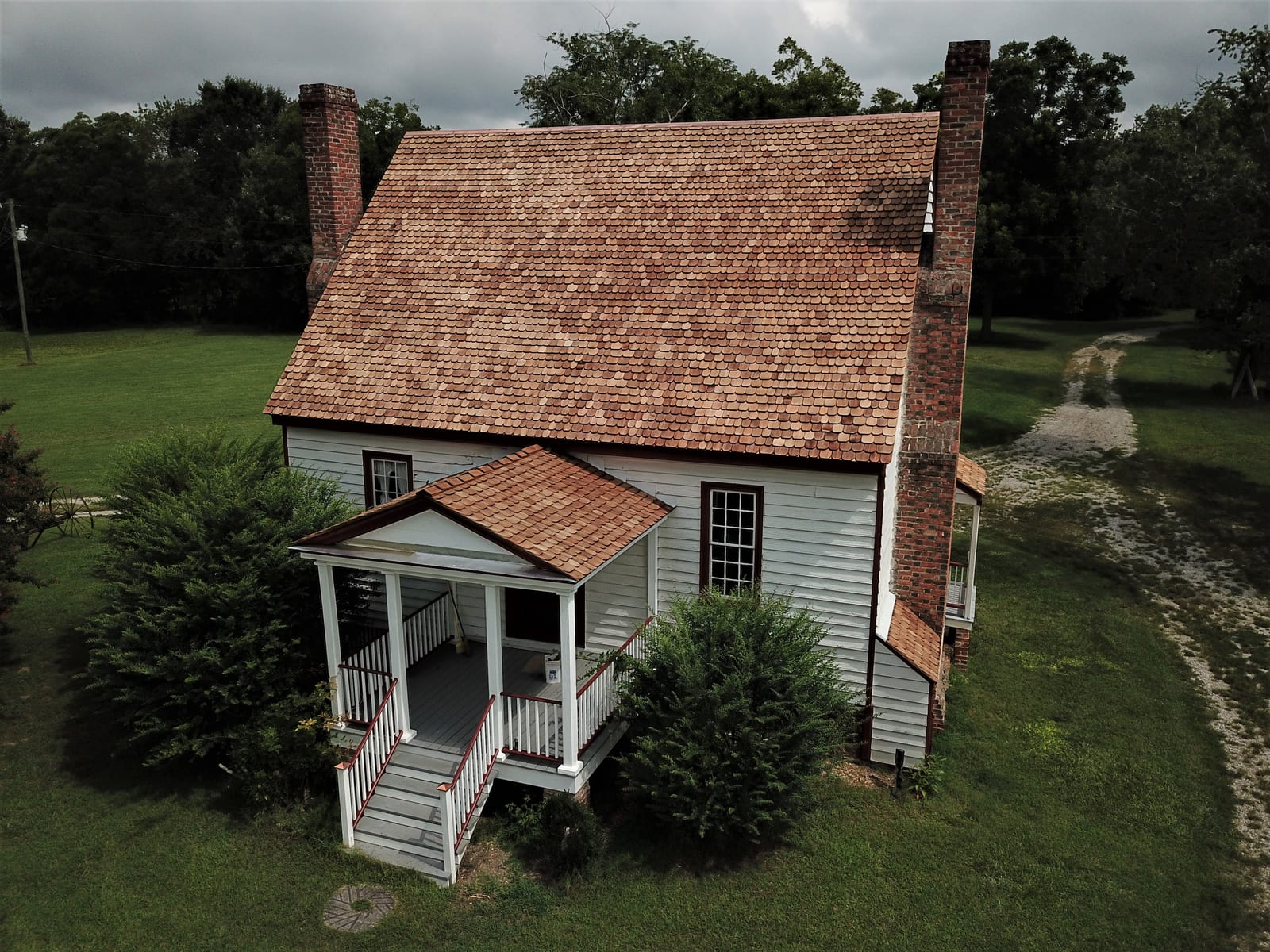 Aerial view of a new cedar shingle roof on a historic farmhouse with a front porch roof