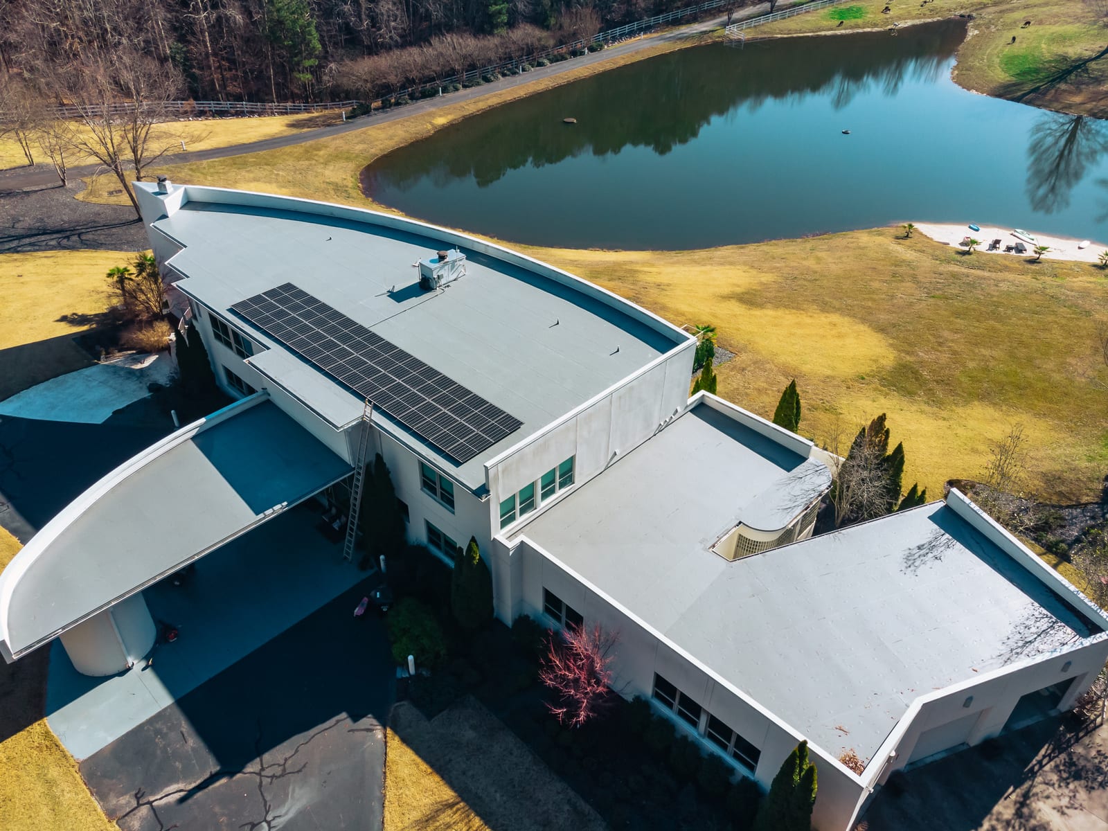 Low-slope membrane roofs on the wings of a modern home beside a pond