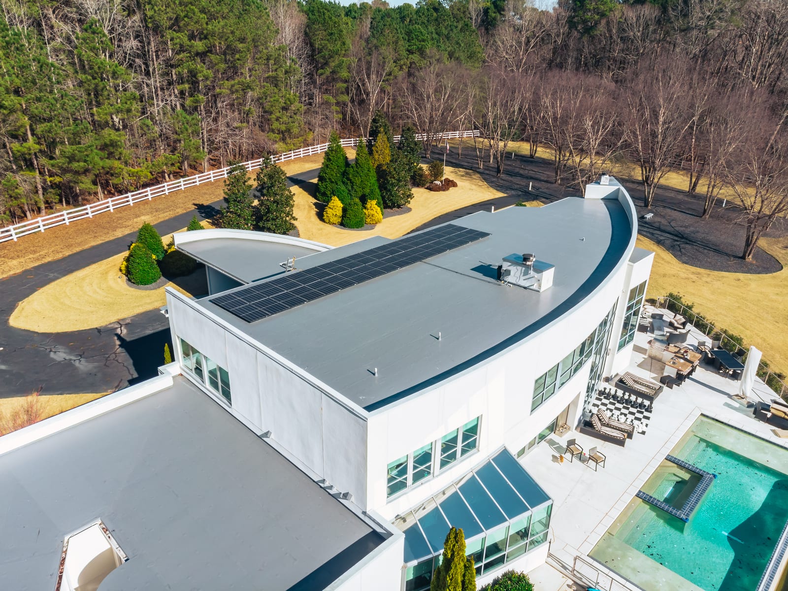 Light gray membrane flat roof with a solar array on a curved modern home above a pool terrace