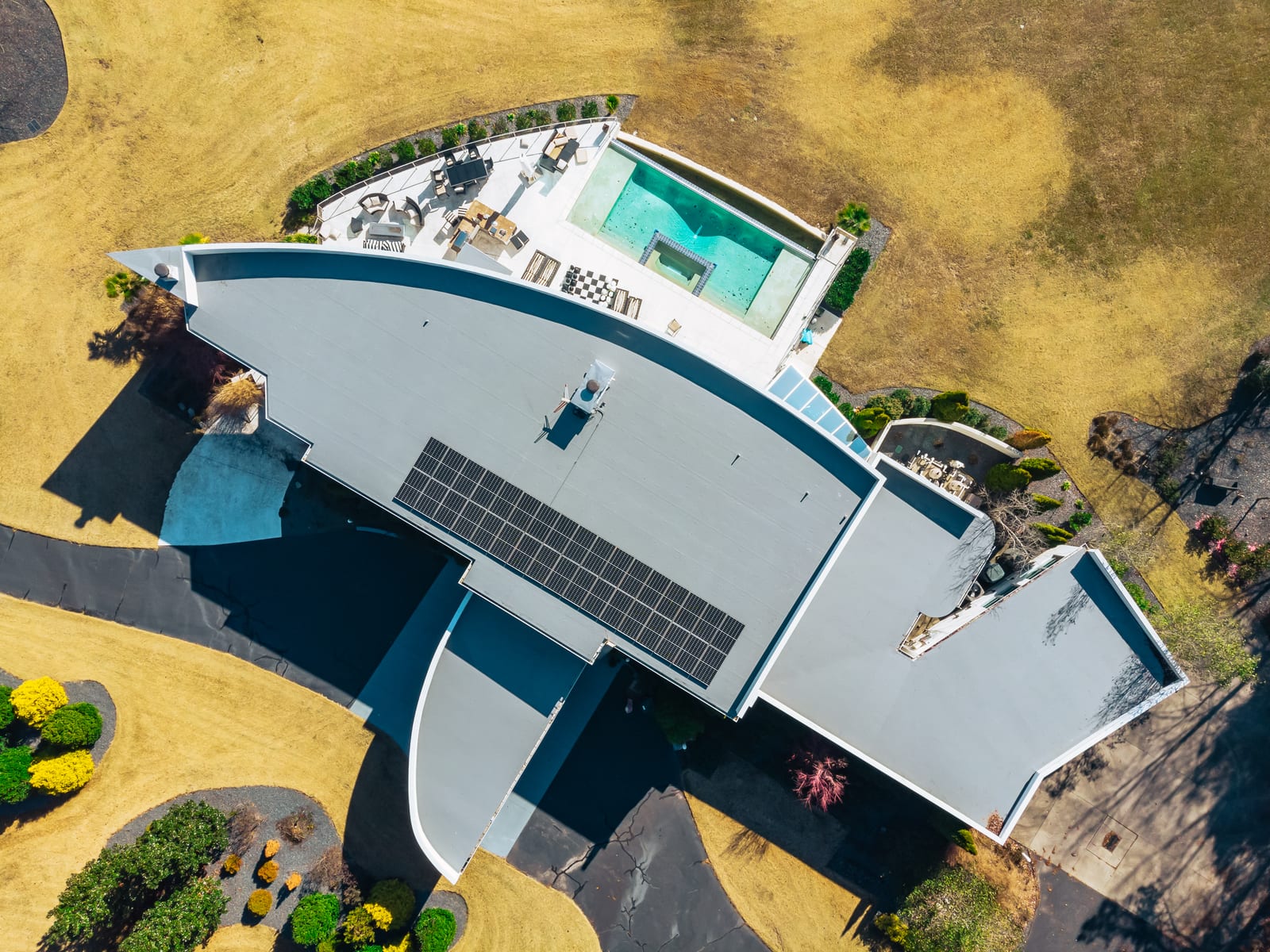 Overhead drone view of a modern home with a gray membrane flat roof, solar panels, and a pool