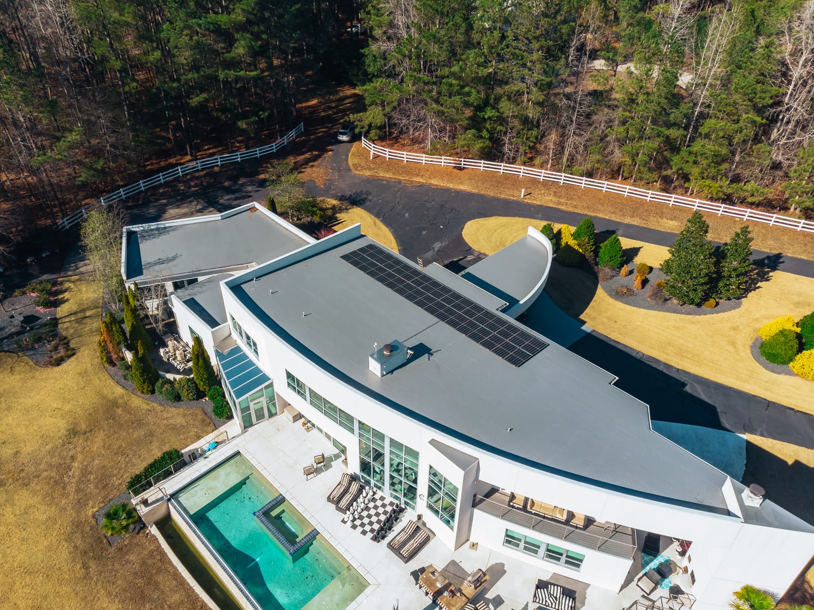 Aerial view of a modern flat-roofed home with a membrane roof, pool, and stone terrace