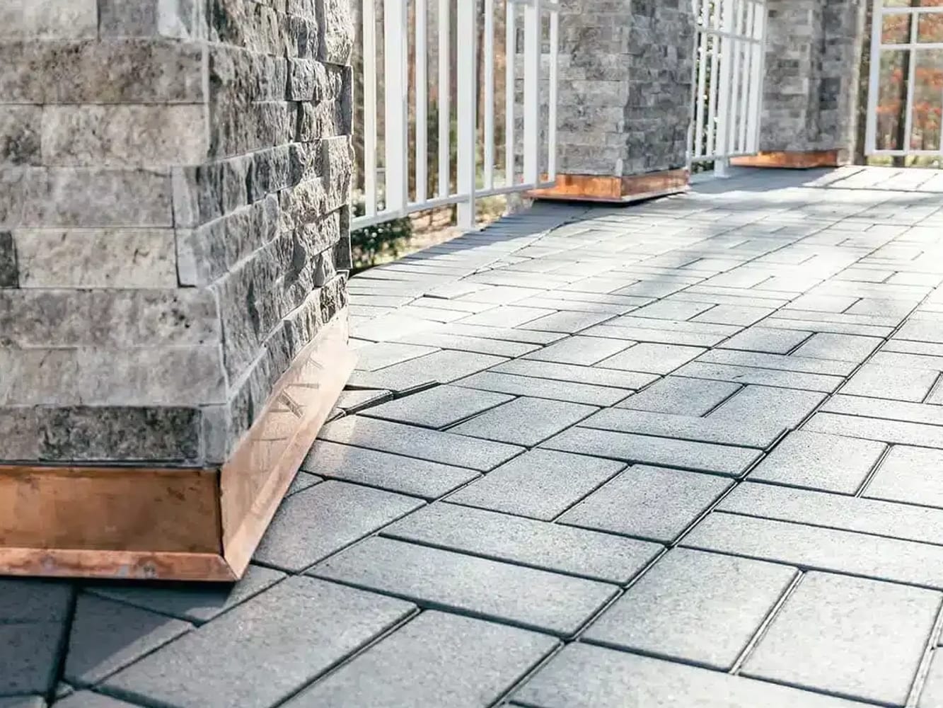 Composite roof deck pavers meeting stone-clad columns with copper base flashing
