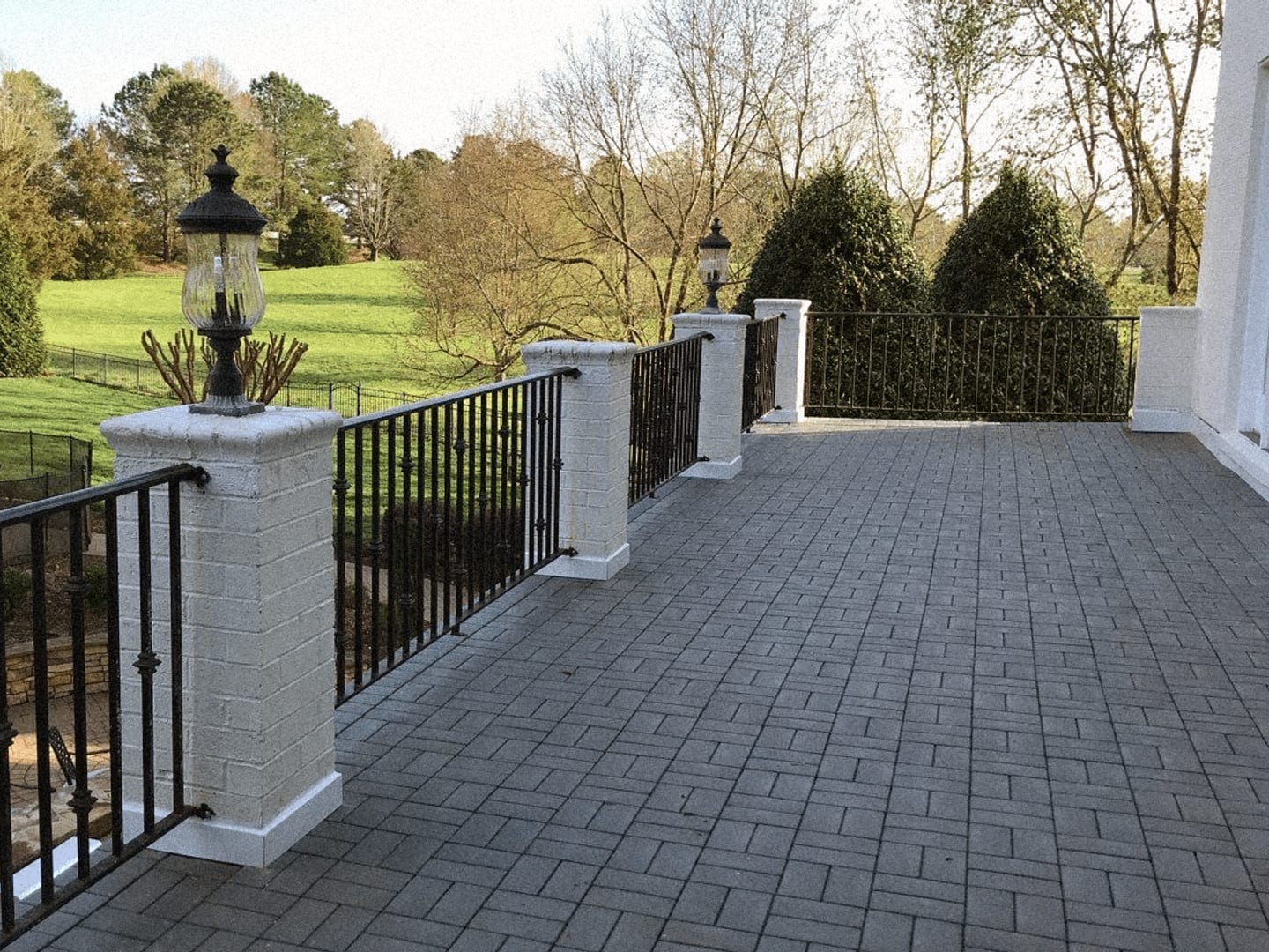 Gray composite roof deck pavers on a large terrace with brick piers and iron railings overlooking a lawn