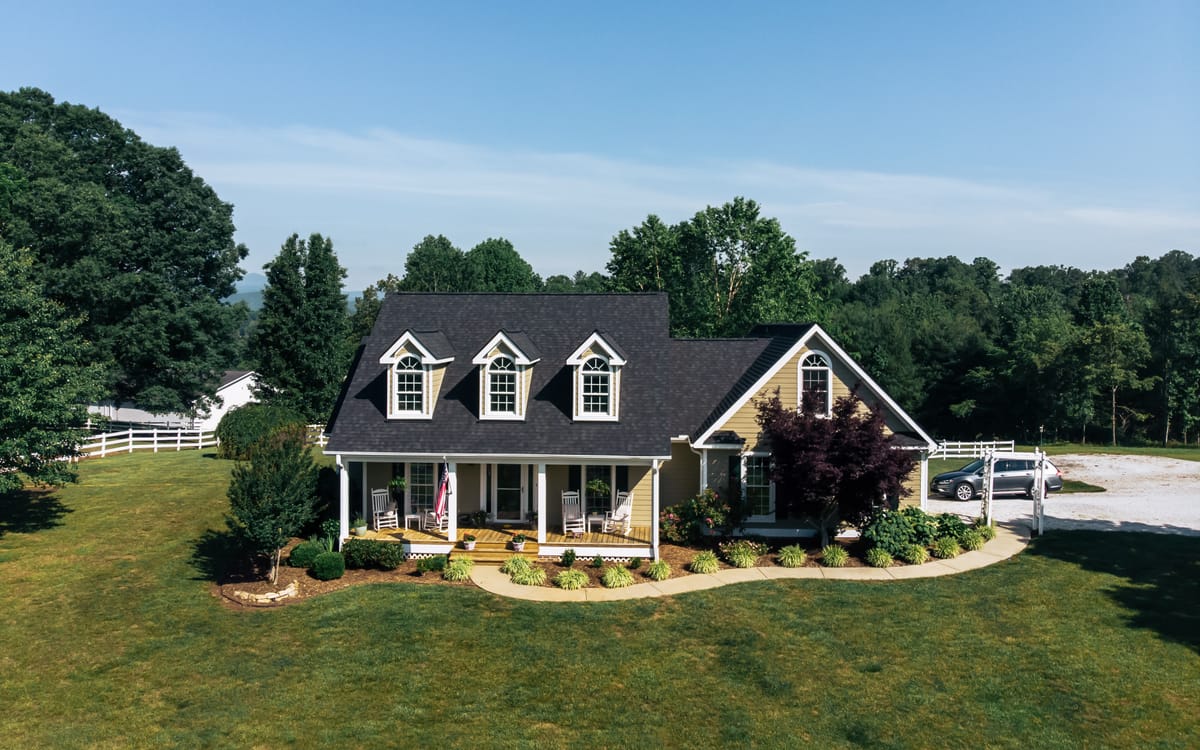 Charcoal shingle roof with three dormers on a farmhouse behind a white fence