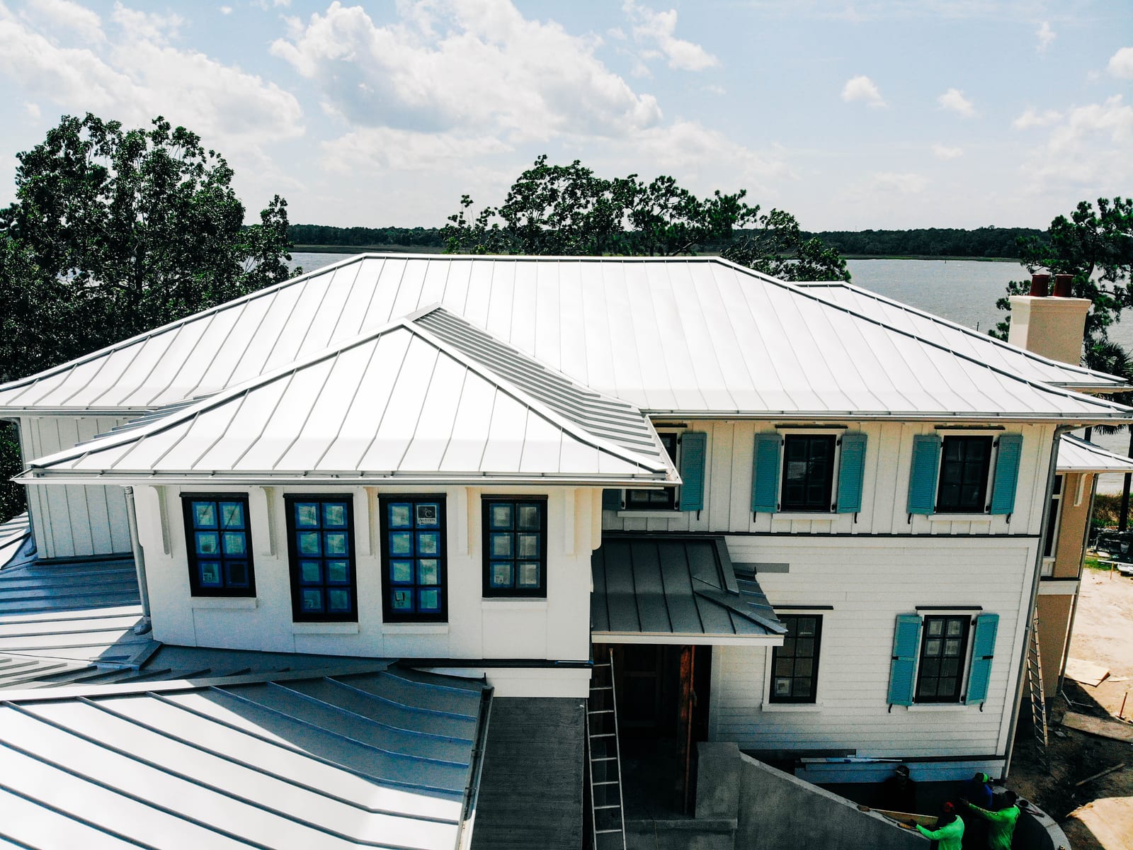 Silver standing seam metal roof on a white home with teal shutters near the water