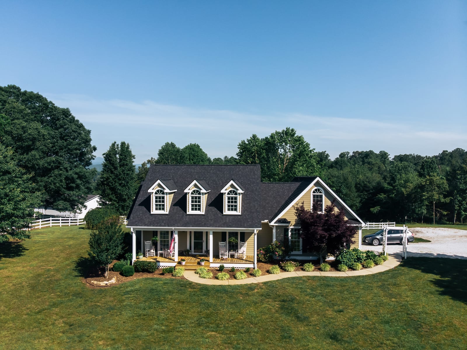 Charcoal shingle roof with three dormers on a farmhouse behind a white fence