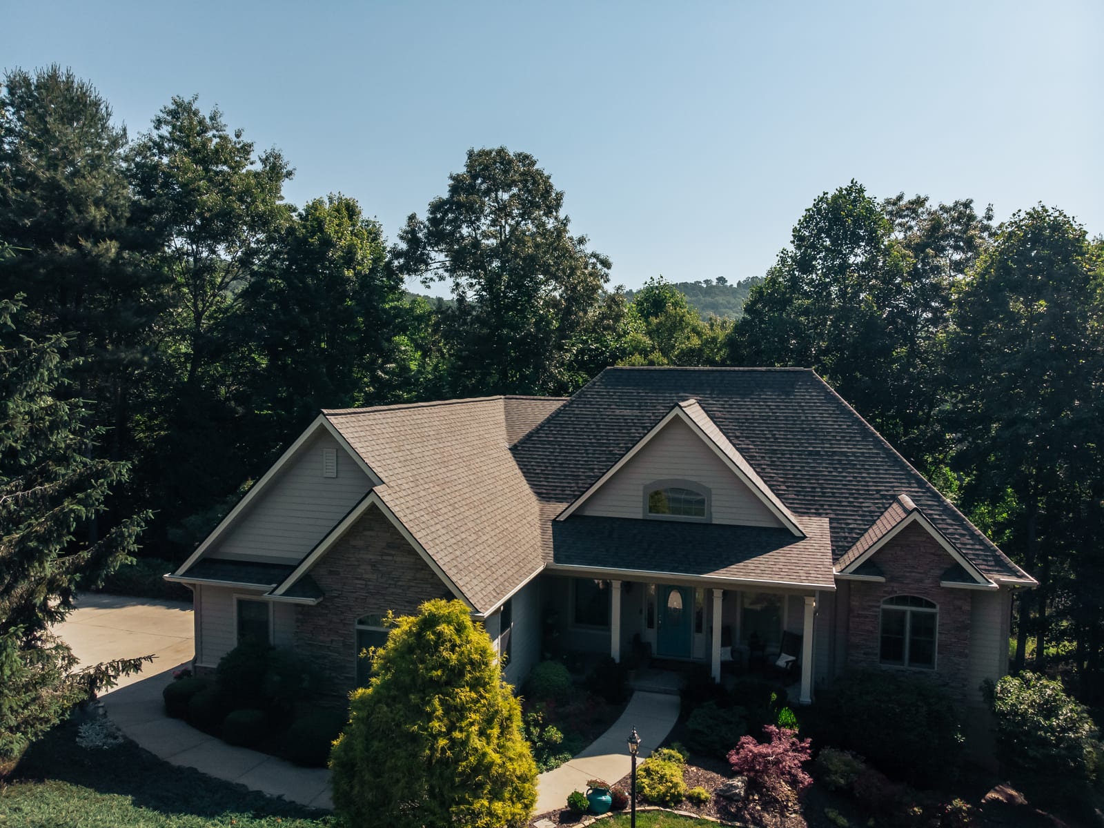 Architectural shingle roof on a stone and siding home with mountains behind it