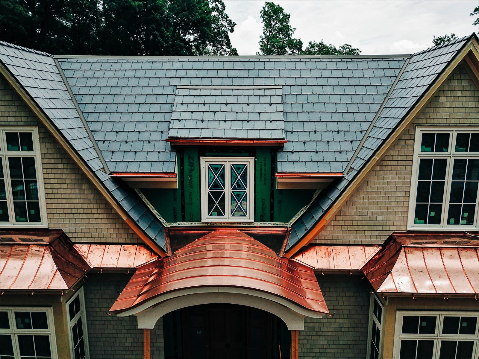 Gray slate roof above standing-seam copper bay roofs and an arched copper entry roof on a shingle-style home