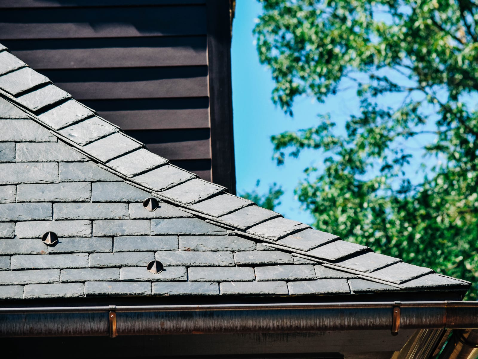 Close-up of a slate roof edge with snow guards above a copper half-round gutter