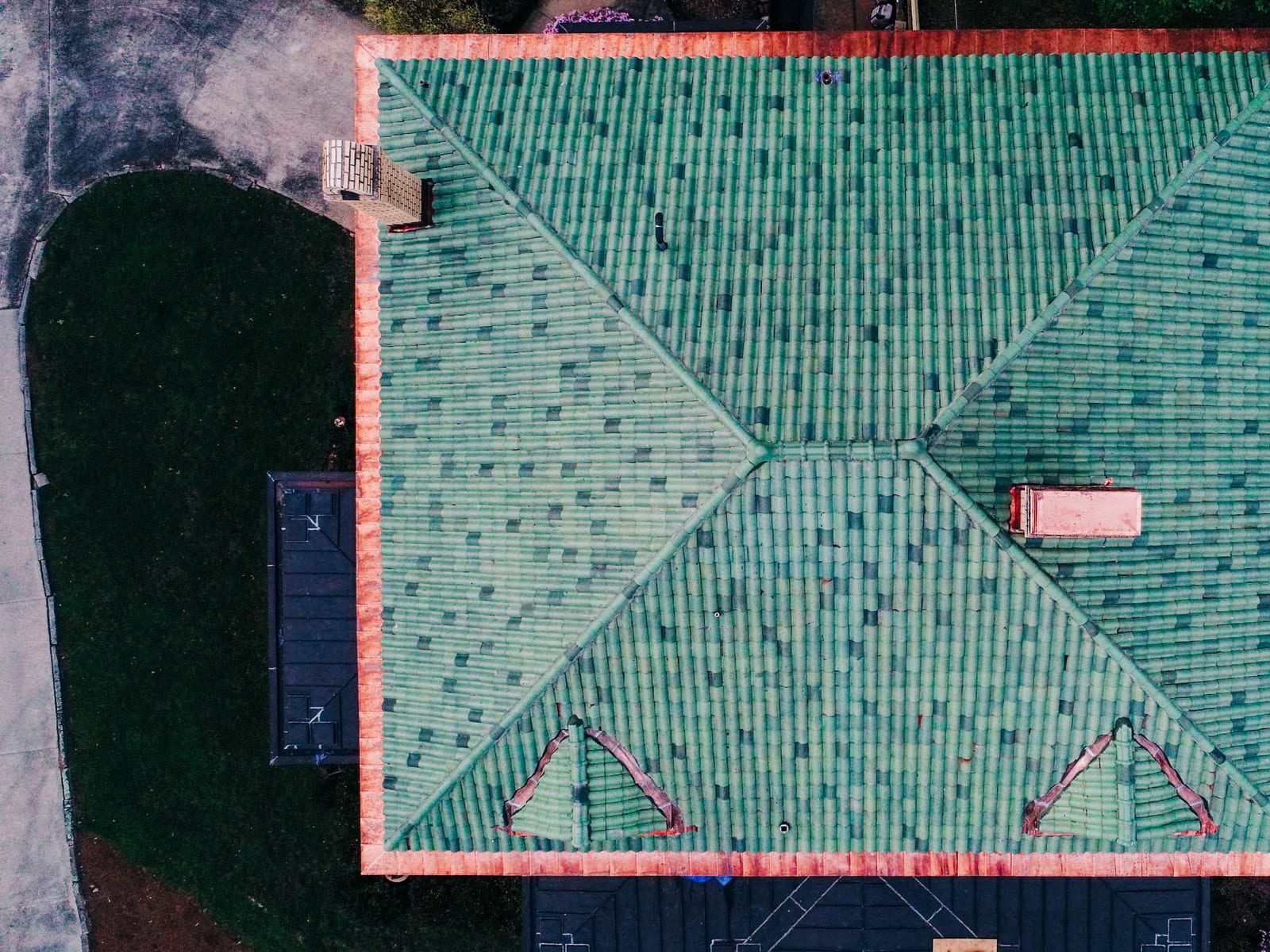 Overhead drone view of a green clay barrel tile hip roof with copper trim at the eaves