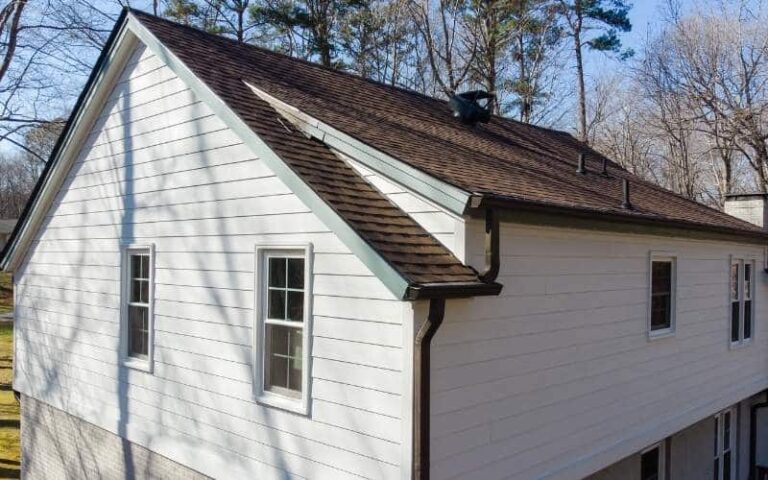 aerial photo of a home with white siding, brown roof, and brown gutters