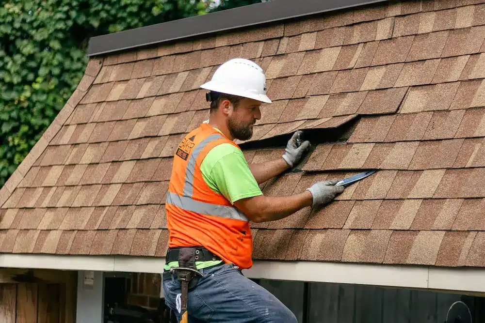 Roofer inspects shingle roof for damage